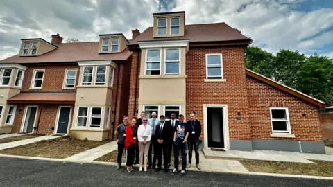 A group of men and women stand outside a large building which is being used to provide homeless people with somewhere to live