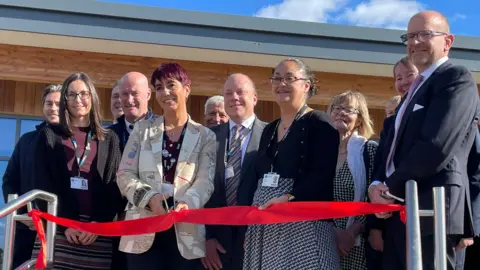 BBC The ribbon cutting ceremony with dignitaries gathered behind a red ribbon with some shiny scissors being brandished