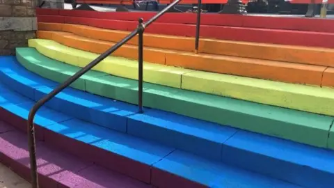 BBC A set of stairs, each one painted a different colour of the rainbow