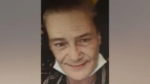 Carol Mighall, wearing a dark dress with a white collar, smiles for the camera in a photo released by her family