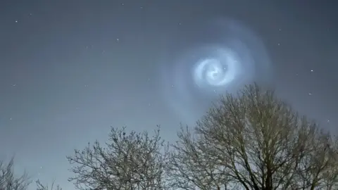 A spiral light in the sky over Asfordby in Leicester. The tops of three trees can also be seen in the image 