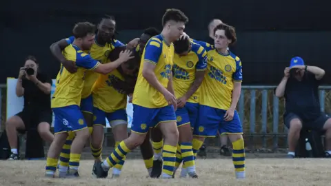 Matt Jarrett Members of the men's Cwmbran AFC side gathered together on the pitch during the game. The kit is blue and yellow with super furry animals written on the front