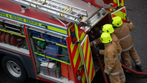 Firefighters fix hoses at the back of their fire engine.