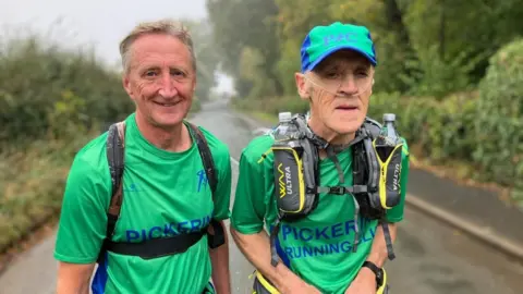 Two men in Pickering Running Club T shirts out on a run. One has medical tubes into his nose