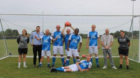 Session participants and coaches pose in full football kit in front of some goals