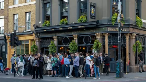 Getty Images The exterior of a Victorian London pub with crowds of people standing outside enjoying a drink. 