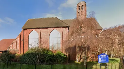 Google Google streetview of All Saints Church as seen from William Street in Kettering on a sunny day. The churh has large windows and a brick turret.