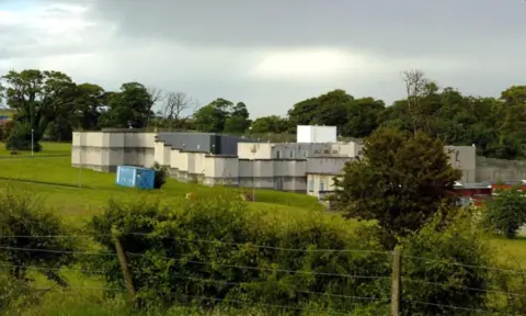 PA Media Landscape photo of Kerelaw Residential School in Stevenston, North Ayrshire. The school is gray and white with a flat roof and is depicted behind a fence and a row of hedges, with a row of trees in the background.