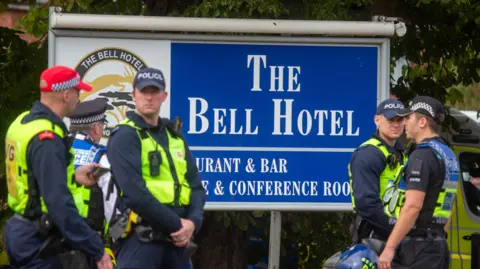 EPA/Shutterstock police officers stand in front of a large blue sign with dark uniform and navy wearing hi-vis vests: "Bell hotel".
