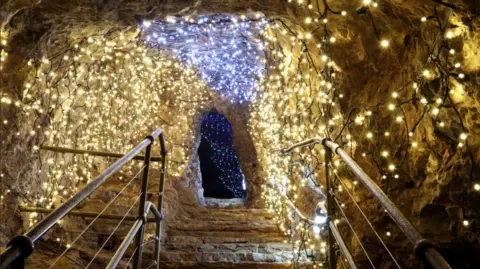 Charlotte Harris A view from the bottom of a set of stairs looking up at a cave entrance in Wookey Hole that has been decorated with loads of fair lights