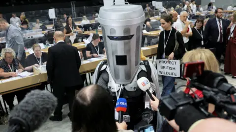 Count Binface, a man dressed as a bin with head covered, speaks to members of the press