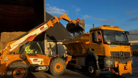 A dumper loads salt into a gritting lorry 