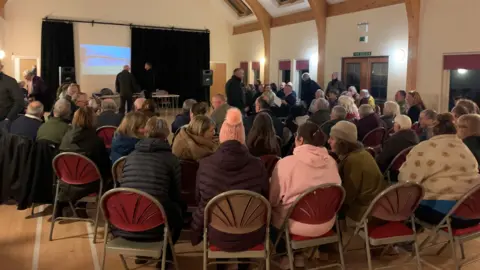 A group of people with their backs to the camera sit on chairs at a meeting in Invergarry.