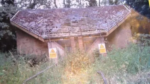 The Drovers Return Cafe An old building, with danger keep out signs, a damaged roof, and lots of foliage all around it. 