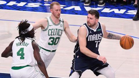 Luca Doncic controls the ball against Boston Celtics pair Sam Hauser and Jrue Holiday