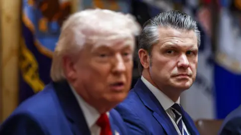 Donald Trump, in a blue suit and bright red neck tie, next to Pete Hegseth, wearing a similar blue suit and blue and white striped neck tie, during a meeting at the White House.