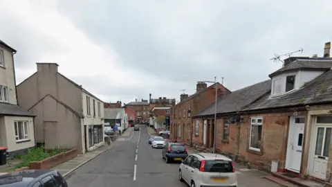 Google A street view of Lady Street in Annan with sandstone buildings down the right hand side and more modern properties down the left. There are cars parked and a grey sky overhead.