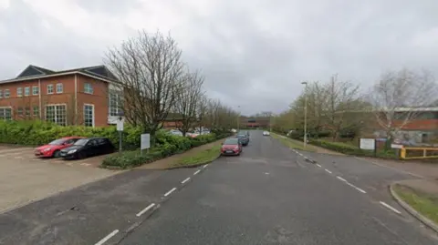 A view of Harvest Crescent on a cloudy day. A few cars are parked by the business units.