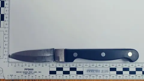 Crown Prosecution Service A black handled kitchen knife with a broken blade and a bent tip next to a ruler measuring the whole object at 195mm long