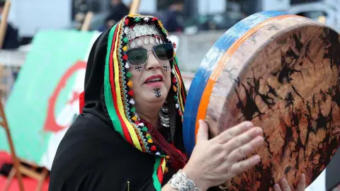 APP/NurPhoto via Getty Images A women with a black, multi-coloured headscarf plays a percussive instrument