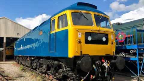 A bright blue and yellow old fashioned train in a shed.