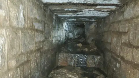 Derbyshire County Council Inside the culvert, seemingly made from stone blocks joined by mortar, showing water trickling through the tunnel