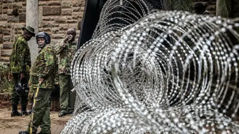  Coils of razor wire are stacked outside a government building as armed security officers stand guard