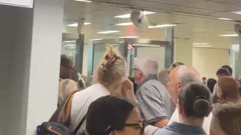 Image shows a large queue of people at Milan's Linate airport