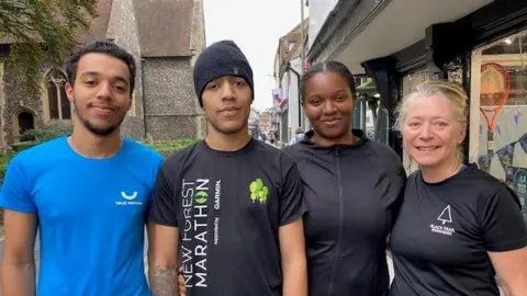 Myles Sarpong (second from left) his brother Lewis (far left), girlfriend Hannah and mum Nina. All bar Lewis left are wearing black tops. There is a church in the background behind them.