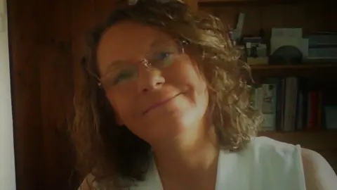 Many Willis A smiling Mandy Willis tilts her head to one side. She has shoulder length brown wavy hair and glasses.