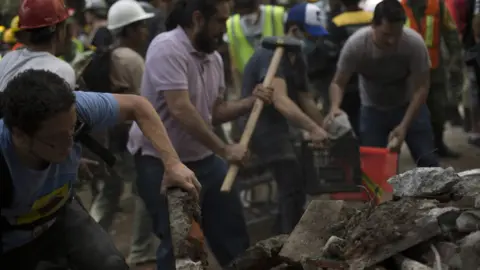 Getty Images Rescuers and volunteers remove rubble and debris from a flattened building in search of survivors after a powerful quake in Mexico City on September 19, 2017.