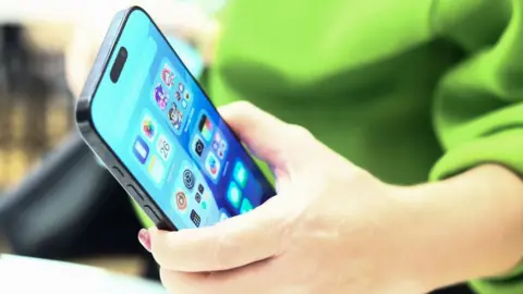 iPhone AI information alerts halted after errors Getty Images Close-up of Apple iPhone 16 held in a person's hand. The person has a green top on.