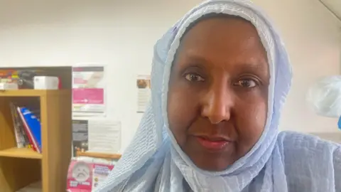 A Somali woman wearing a light blue hijab looks into the camera from an office