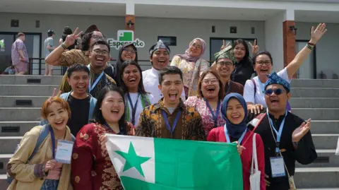 Indonesian Esperanto Youth Organization (IEJO) A group of people smile for the camera holding a flag representing the Esperanto language.