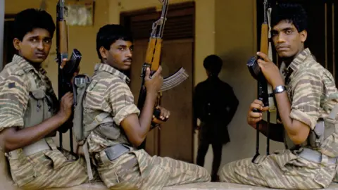 Getty Images Three Tamil Tiger fighters pose in their uniform with guns