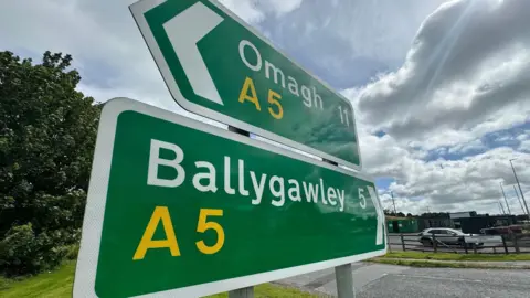 A sign for the A5 road in County Tyrone. Two green signs one above the other point in opposite directions, one pointed towards Omagh, the other Ballygawley 