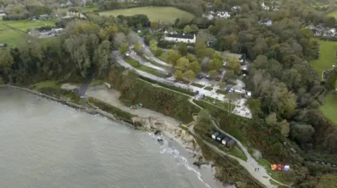Aerial view of Middle Beach which is surrounded by trees. The tide is in. Behind the beach is a car park and beyond that are a number of houses.