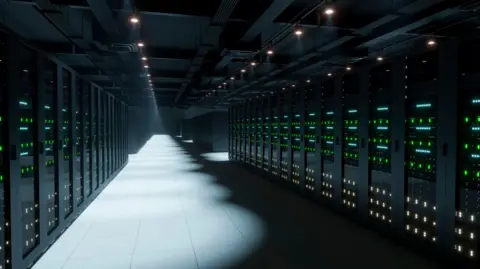 Rows of computer servers with LED lights fill a dark room. The floor tiles and some of the systems are illuminated by spotlighting.