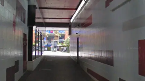 A picture taken inside the underground subway of Friary Passage in Guildford, showing red and white tiles on the walls and daylight at the end of the passage.