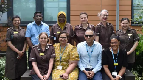 Two rows of staff members - one row is standing and one row is sitting, with Poonam sitting in the middle, wearing a yellow dress.
