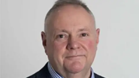 A man with short grey hair pictured from the shoulders up against a white background