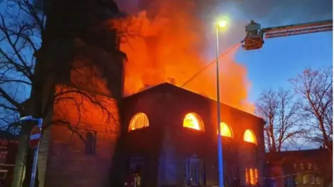 A fire engine turntable ladder uses a hose to extinguish a large fire at St John's Church in Blackburn.