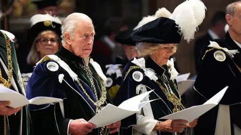 Getty Images Queen Camilla and King Charles III attend the Thistle Service at St Giles' Cathedral. They are in ceremonial robes and are singing from sheets.