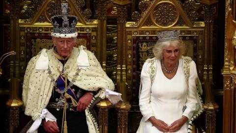 King Charles and Queen Camilla in full regalia sitting on thrones