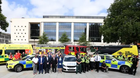Paul Nicholls A group of people at Kings Square surrounded by ambulances, fire engines and police cars.