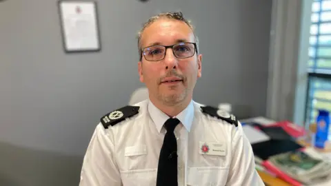 Assistant Chief Constable Richard Ocone sitting in an office. He is wearing uniform and black glasses.