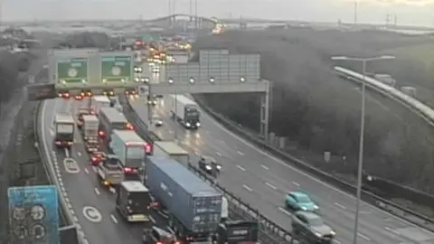 Traffic queuing on the A282 in rain, below a gantry with large green signs