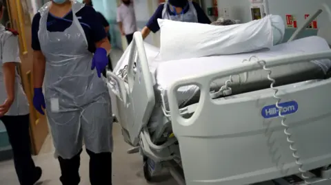 PA Hospital staff move around a patient on a trolley in a hospital corridor