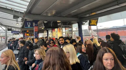Passengers crowd on a train platform at Manchester Piccadilly station.