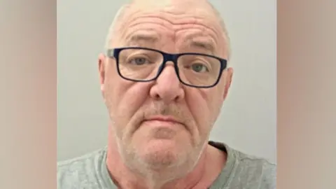 Police handout Police custody image of David Berry with receding grey hair and grey beard wearing black glasses and grey t-shirt.
